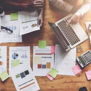 Marketing concept: papers with graphs and charts on table and a person working on a laptop